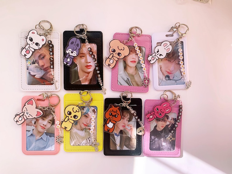 May include: Seven colorful ID card holders with keychains. Each holder has a different cartoon character charm and a beaded chain with a name on it. The holders are pink, white, black, yellow, and light pink.