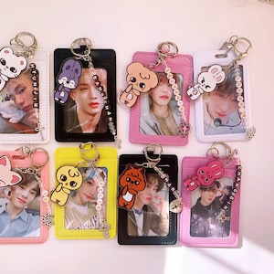 May include: Set of ten colorful ID card holders with keychains. Each holder features a different cartoon animal and a photo of a person. The holders are made of plastic and have a clear window for displaying an ID card. The keychains are made of metal and have a beaded charm.
