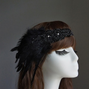 May include: A black headband with a feather and beaded embellishments. The headband is worn on a mannequin with long brown hair.