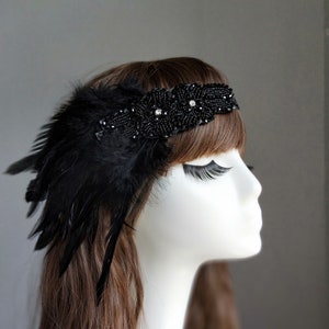 May include: A black headband with black feathers and rhinestones. The headband is worn on a mannequin with brown hair.