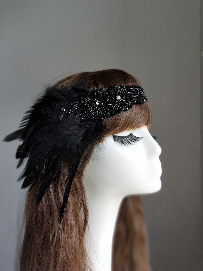 May include: A black headband with black feathers and rhinestones. The headband is worn on a mannequin with brown hair.