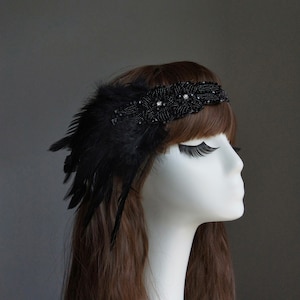 May include: A black headband with black feathers and beaded embellishments. The headband is worn on a mannequin with long brown hair.