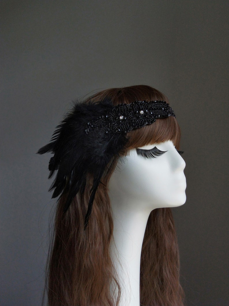 May include: A black headband with black feathers and beaded embellishments. The headband is worn on a mannequin with long brown hair.