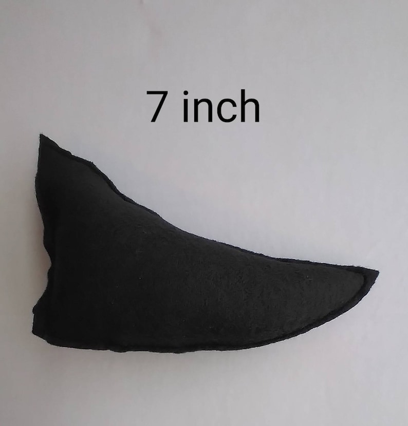 May include: A black felt object, approximately 7 inches in length, against a white background. The object has a curved, pointed shape, with a stitched edge. The text "7 inch" is above the object.
