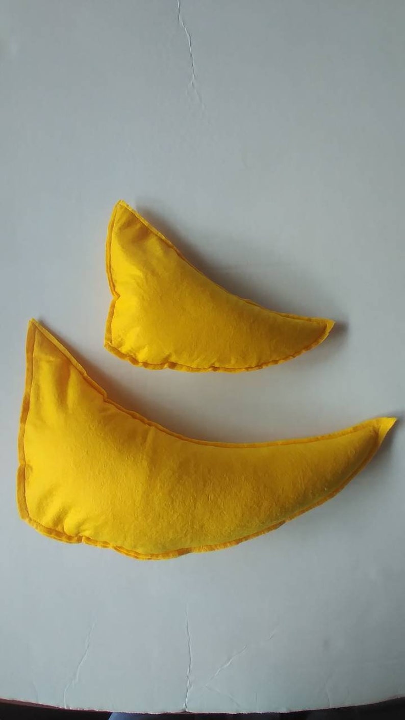 May include: Two yellow crescent-shaped pillows. The pillows are made of a soft fabric and have a contrasting yellow trim. One pillow is larger than the other. The pillows are on a white background.