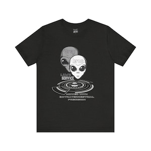 May include: Dark gray t-shirt featuring a graphic of two alien heads with the text "Grey Bros Lawn Service." The design includes a circular pattern and the phrase "Mowed with Extraterrestrial Precision."