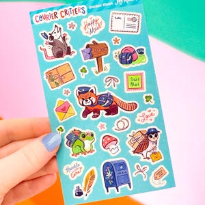 May include: A sticker sheet titled "Courier Critters" featuring various cartoon animals and mail-themed illustrations. The stickers include a rat, snail, red panda, frog, owl, and mailbox, with phrases like "Happy Mail" and "Snail Mail". The sheet is held against a colorful background.