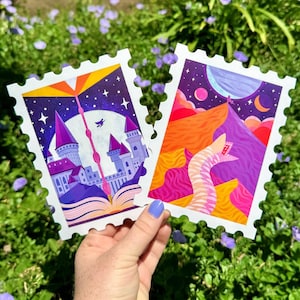 May include: Two illustrated postcards with a whimsical, fairytale theme. The first postcard features a castle with a book open in front of it, with a night sky and stars in the background. The second postcard features a pink and purple creature with a starry night sky in the background.