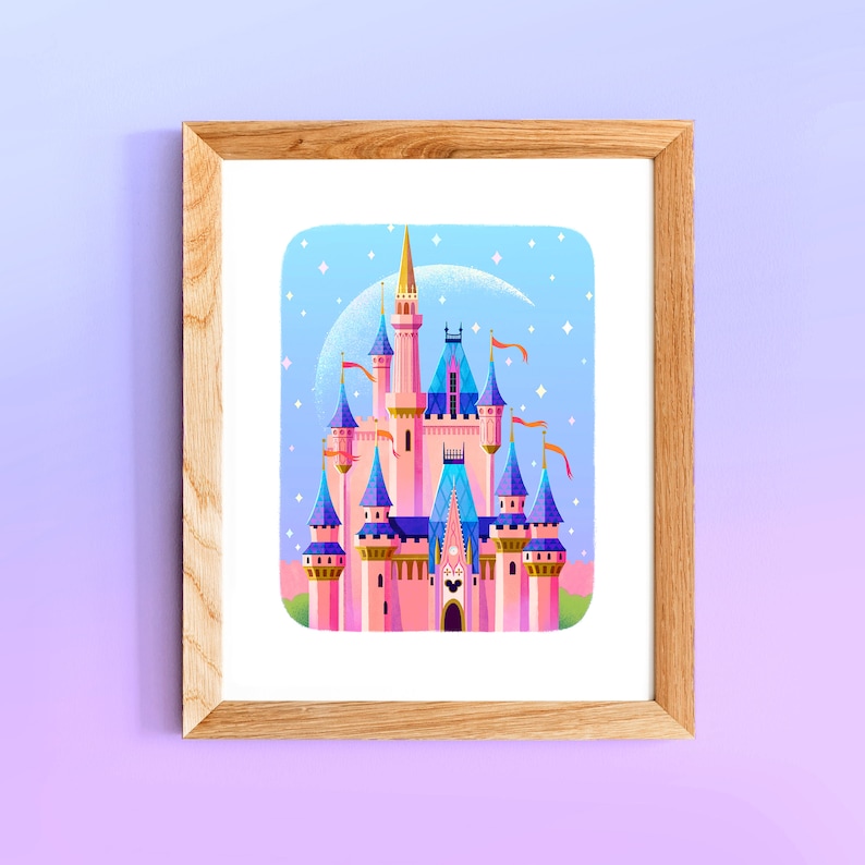 May include: A framed print of a pink and blue castle with a crescent moon and stars in the background. The castle has multiple towers and spires, and the windows are blue. The print is in a light wood frame.