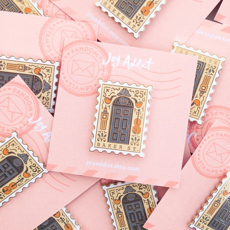 May include: A gold-colored enamel pin shaped like a postage stamp with a black door with gold accents and the text "221B BAKER ST."  The pin is surrounded by a white border with the text "FANDOM STAMPS" and "25".