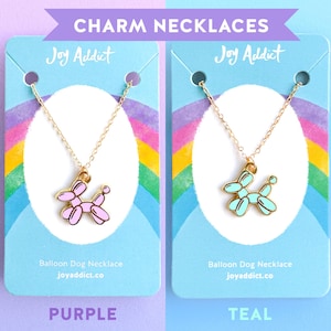 Peut inclure: Deux colliers avec pendentifs en forme de chien ballon. Le collier de gauche a un pendentif en forme de chien ballon violet et le collier de droite a un pendentif en forme de chien ballon turquoise. Les deux colliers sont pr&eacute;sent&eacute;s sur des cartes d'affichage avec le texte "Joy Addict" et "Balloon Dog Necklace" dessus.
