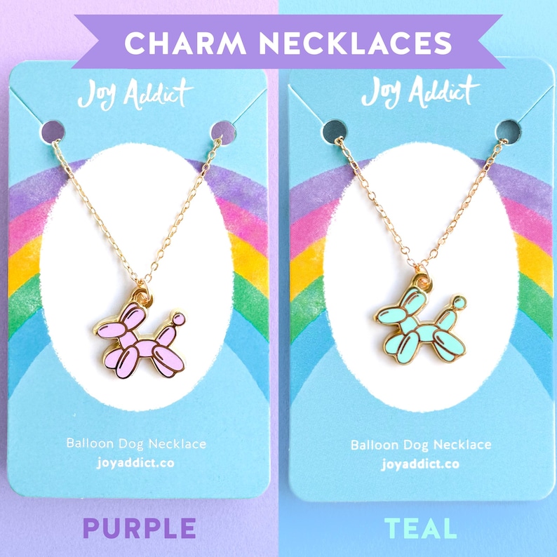 Peut inclure: Deux colliers avec pendentifs en forme de chien ballon. Le collier de gauche a un pendentif en forme de chien ballon violet et le collier de droite a un pendentif en forme de chien ballon turquoise. Les deux colliers sont pr&eacute;sent&eacute;s sur des cartes d'affichage avec le texte "Joy Addict" et "Balloon Dog Necklace" dessus.