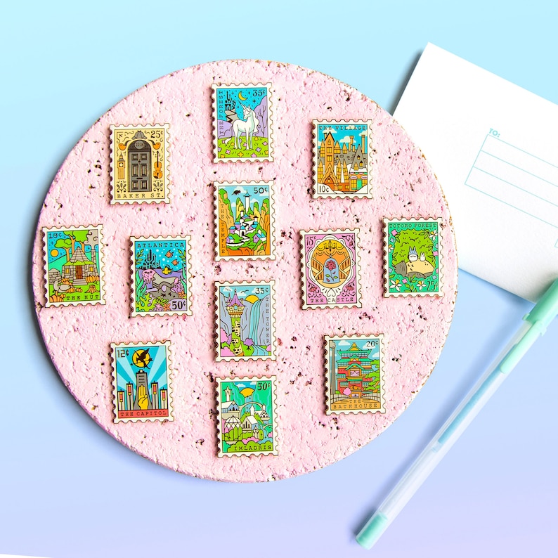 May include: A collection of 10 enamel pins featuring various whimsical illustrations, including a unicorn, a castle, a Totoro, and a cityscape. The pins are arranged on a pink corkboard and resemble postage stamps with different prices.