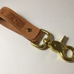 May include: A tan leather key chain with a brass swivel hook. The leather strap has the word "2022" embossed on it.