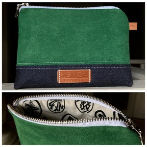 May include: A green zippered pouch with a denim bottom and a brown leather patch that says "MADE PDX, USA". The pouch is open to reveal a white fabric lining with black Japanese characters.