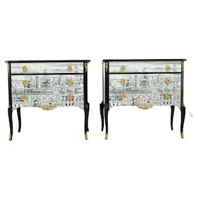 May include: A pair of black and gold painted antique chest of drawers with a white and grey cityscape design.