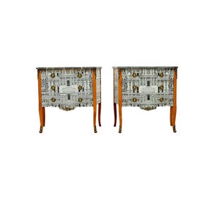 May include: Two matching white and gold painted wooden bedside tables with three drawers each. The drawers have a black and white patterned design.
