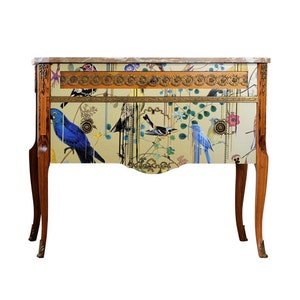 Può includere: Un comò in legno in stile vintage con un motivo a uccelli e fiori. Il comò ha un piano in marmo e dettagli dorati.