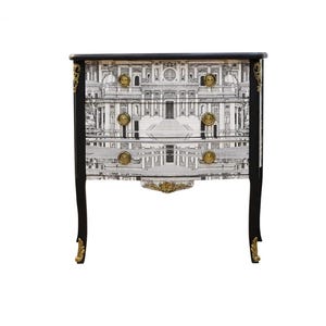 Può includere: Un comò nero con dettagli dorati e un design a motivi bianco e nero. I cassetti presentano una stampa architettonica in bianco e nero.