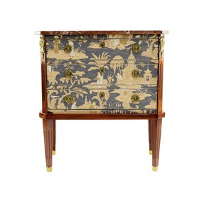 May include: A three-drawer chest with a marble top and gold accents. The drawers are decorated with a blue and gold floral pattern.