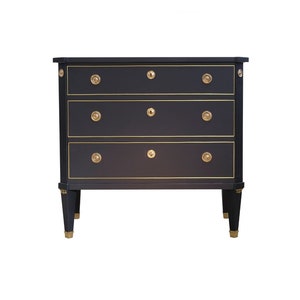 May include: A black chest of drawers with three drawers and gold-toned hardware. The chest of drawers has a simple, elegant design.