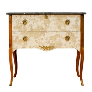 Può includere: Un antico comò a due cassetti con piano in marmo. Il comò è in legno e ha una finitura marrone chiaro. I cassetti hanno un motivo floreale e maniglie in ottone.
