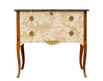 May include: A two-drawer antique chest of drawers with a marble top. The chest is made of wood and has a light brown finish. The drawers have a floral pattern and brass handles.