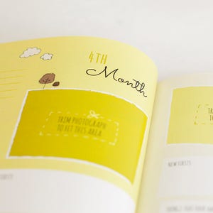 Puede incluir: Un libro de recuerdos para beb&eacute;s de color amarillo con un espacio para fotos para el cuarto mes. La p&aacute;gina tiene un espacio para una foto con el texto "Recortar la fotograf&iacute;a para que quepa en esta &aacute;rea" y una lista de verificaci&oacute;n.