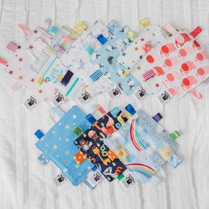 Puede incluir: Una colecci&oacute;n de diez mantas de etiquetas para beb&eacute;s de colores vivos con varios patrones, incluyendo estrellas, arco&iacute;ris, animales y dise&ntilde;os geom&eacute;tricos. Las mantas est&aacute;n hechas de tela suave y tienen cintas de sat&eacute;n atadas a las esquinas.