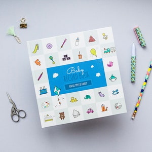 K&ouml;nnte beinhalten: Ein blaues und wei&szlig;es Baby-Erinnerungsbuch mit dem Titel "Baby Record Book" und dem Text "F&uuml;r alle Arten von Familien". Der Umschlag zeigt eine Vielzahl von bunten Illustrationen von Babyartikeln, wie eine Rassel, einen Schnuller, einen Spielzeugzug und einen Teddyb&auml;r.