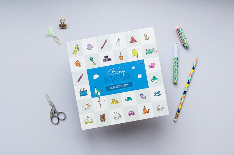 K&ouml;nnte beinhalten: Ein blaues und wei&szlig;es Baby-Erinnerungsbuch mit dem Titel "Baby Record Book" und dem Text "F&uuml;r alle Arten von Familien". Der Umschlag zeigt eine Vielzahl von bunten Illustrationen von Babyartikeln, wie eine Rassel, einen Schnuller, einen Spielzeugzug und einen Teddyb&auml;r.