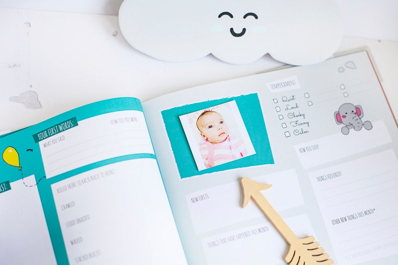 Puede incluir: Un libro de recuerdos para beb&eacute;s con una cubierta azul turquesa y una foto de una ni&ntilde;a peque&ntilde;a en la p&aacute;gina. La p&aacute;gina tiene secciones para registrar las primeras palabras del beb&eacute;, c&oacute;mo se mueve el beb&eacute;, su temperamento y sus nuevos dientes.