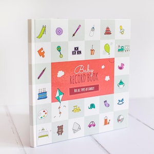 K&ouml;nnte beinhalten: Ein wei&szlig;es Baby-Erinnerungsbuch mit einem rot-wei&szlig;en Titel, der "Baby Record Book" und die Worte "F&uuml;r alle Arten von Familien" lautet. Der Einband ist mit bunten Illustrationen von Babyartikeln wie einer Rassel, einem Schnuller, einem Spielzeugzug und einem Drachen verziert.