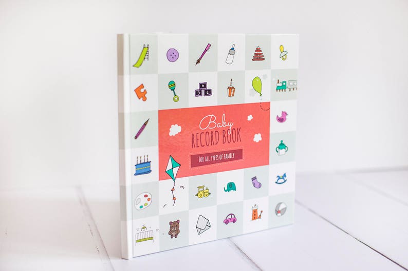 K&ouml;nnte beinhalten: Ein wei&szlig;es Baby-Erinnerungsbuch mit einem rot-wei&szlig;en Titel, der "Baby Record Book" und die Worte "F&uuml;r alle Arten von Familien" lautet. Der Einband ist mit bunten Illustrationen von Babyartikeln wie einer Rassel, einem Schnuller, einem Spielzeugzug und einem Drachen verziert.