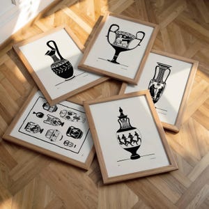 May include: Five framed black and white prints of ancient Greek pottery. The prints are in light brown wooden frames and are arranged on a wooden floor. The pottery designs include vases and urns with intricate patterns and figures.