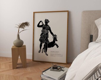 May include: A framed black and white print featuring a classical illustration of Artemis/Diana with a deer. The artwork is displayed in a light-colored wooden frame, leaning against a wall. The print is on a beige background.