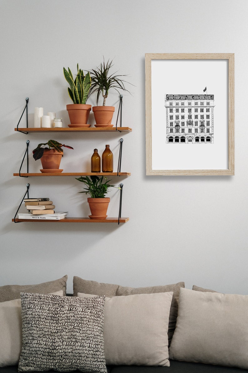 Puede incluir: Tres estantes de madera con soportes de metal negro est&aacute;n montados en una pared blanca. Los estantes est&aacute;n decorados con plantas en macetas, libros y botellas de vidrio. Un dibujo en blanco y negro de un edificio enmarcado cuelga de la pared sobre los estantes.