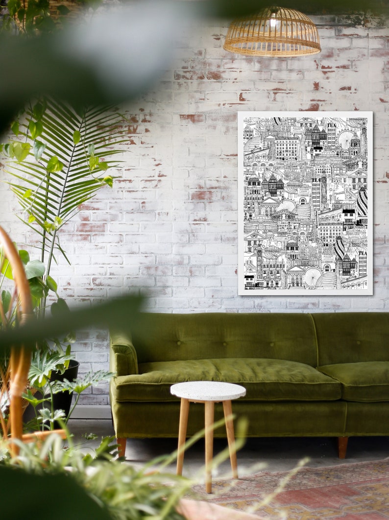 K&ouml;nnte beinhalten: Eine Schwarz-Wei&szlig;-Zeichnung einer Stadtlandschaft, gedruckt auf einem wei&szlig;en Poster, das an einer wei&szlig;en Backsteinwand &uuml;ber einem gr&uuml;nen Samtsofa und einem kleinen wei&szlig;en Holztisch h&auml;ngt.