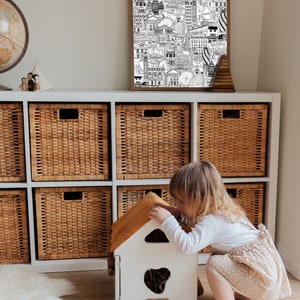 K&ouml;nnte beinhalten: Ein wei&szlig;es und braunes Holzspielzeughaus mit einem kleinen Fenster und einem braunen Dach. Ein kleines Kind spielt mit dem Spielzeughaus.