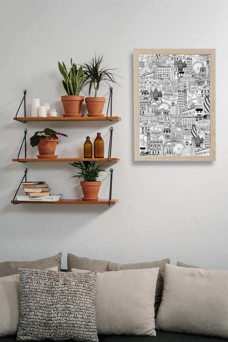 K&ouml;nnte beinhalten: Drei Holzregale mit schwarzen Metallhalterungen sind an einer wei&szlig;en Wand montiert. Die Regale sind mit Topfpflanzen, Kerzen, B&uuml;chern und zwei Glasflaschen dekoriert. Ein gerahmtes Schwarzwei&szlig;-Strichbild einer Stadtkulisse h&auml;ngt an der Wand &uuml;ber den Regalen.