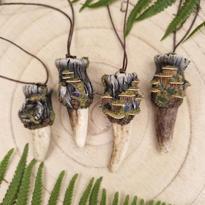 May include: Four pendants on dark brown cords, each featuring a sculpted, textured base resembling a tree stump or rock formation adorned with miniature fungi, moss, and small crystals, attached to a smooth, tapered, off-white horn-like point.