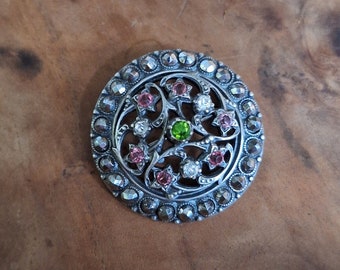Broche Belle Epoque ronde ajourée en métal argenté (?) avec marcassites et pierres rose blanches et verte