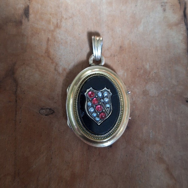 Pendentif porte-photo XIX ovale en plaqué or avec médaillon noir en onyx ? présentant un blason doré serti de perles fines et pierres roses