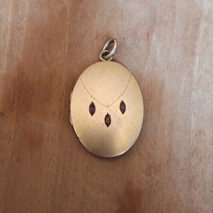 Può includere: Un medaglione d'oro con un design a catena e tre pietre preziose rosse.