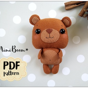 May include: A handmade brown felt bear with a light brown muzzle, ears, and belly. The bear has black button eyes and a stitched smile. The image includes the text "Mimi Boom" and "PDF pattern".