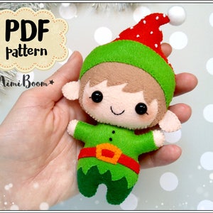 May include: A handmade felt elf doll with a green tunic, red belt, and red and green hat. The doll has a smiling face with black button eyes and is holding its arms out. The text "PDF pattern" and "MimiBoom" are visible.