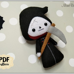 May include: A handmade felt Grim Reaper doll with a black hooded robe, holding a gray scythe. The doll has a white skull face with black eyes and a red collar. The image includes a PDF pattern label and a felt bat.