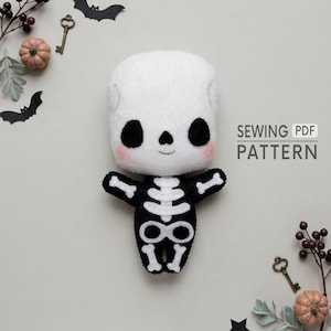 Puede incluir: Un muñeco esqueleto de peluche con cabeza blanca, cuencas oculares negras y mejillas rosadas. El cuerpo es negro con detalles de huesos en fieltro blanco. El texto SEWING PDF PATTERN es visible, junto a llaves y murciélagos decorativos.