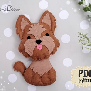 May include: A brown felt Yorkshire Terrier dog plush toy with pink tongue and black eyes. The toy is sitting on a gray background with white polka dots. The text "PDF pattern" is in a brown cloud shape.