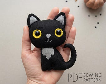 May include: A black felt cat plush toy with large yellow eyes, a light gray nose, and a light gray chest patch. The cat has pointed ears with light gray inner details and a curved tail. The text PDF SEWING PATTERN is visible in the corner.